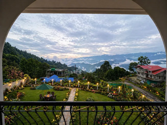 The view from a room balcony over the lit garden toward layered hills at dusk