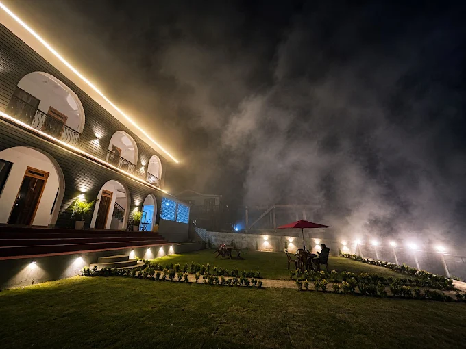 The heritage house after dark, its arches strung with warm light, mist rolling across the lawn